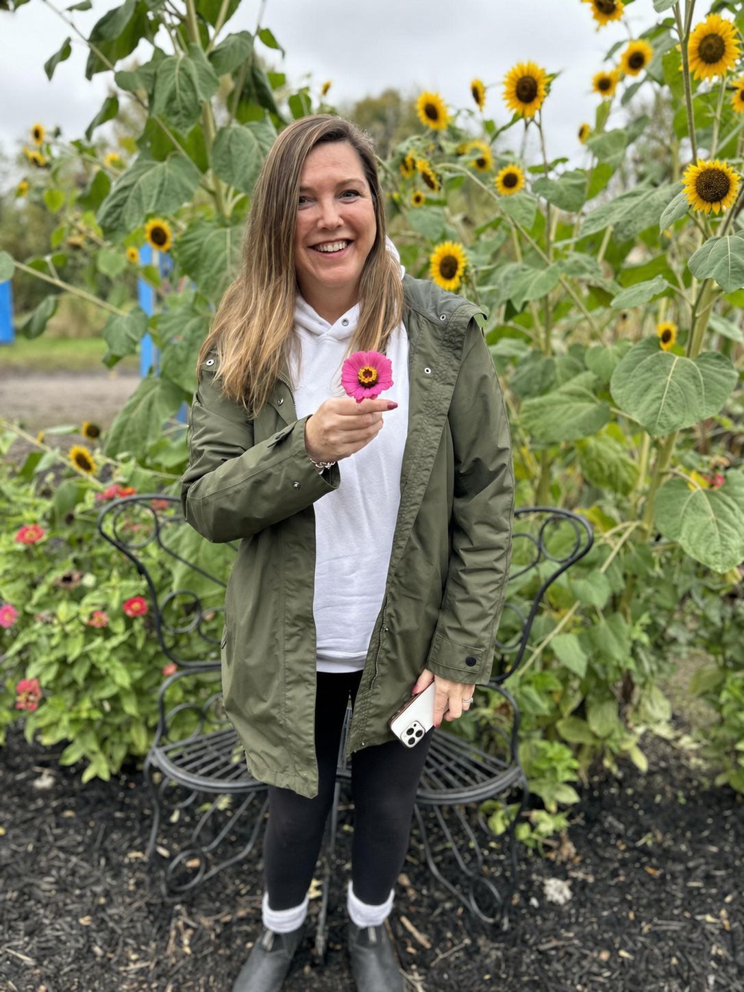 Karen smiling in a sunflower garden, holding a pink zinnia
